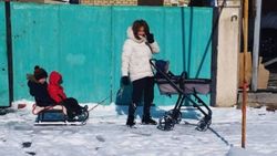 Девушка с ребенком в коляске тянет санки, на которых еще двое детей. Фото