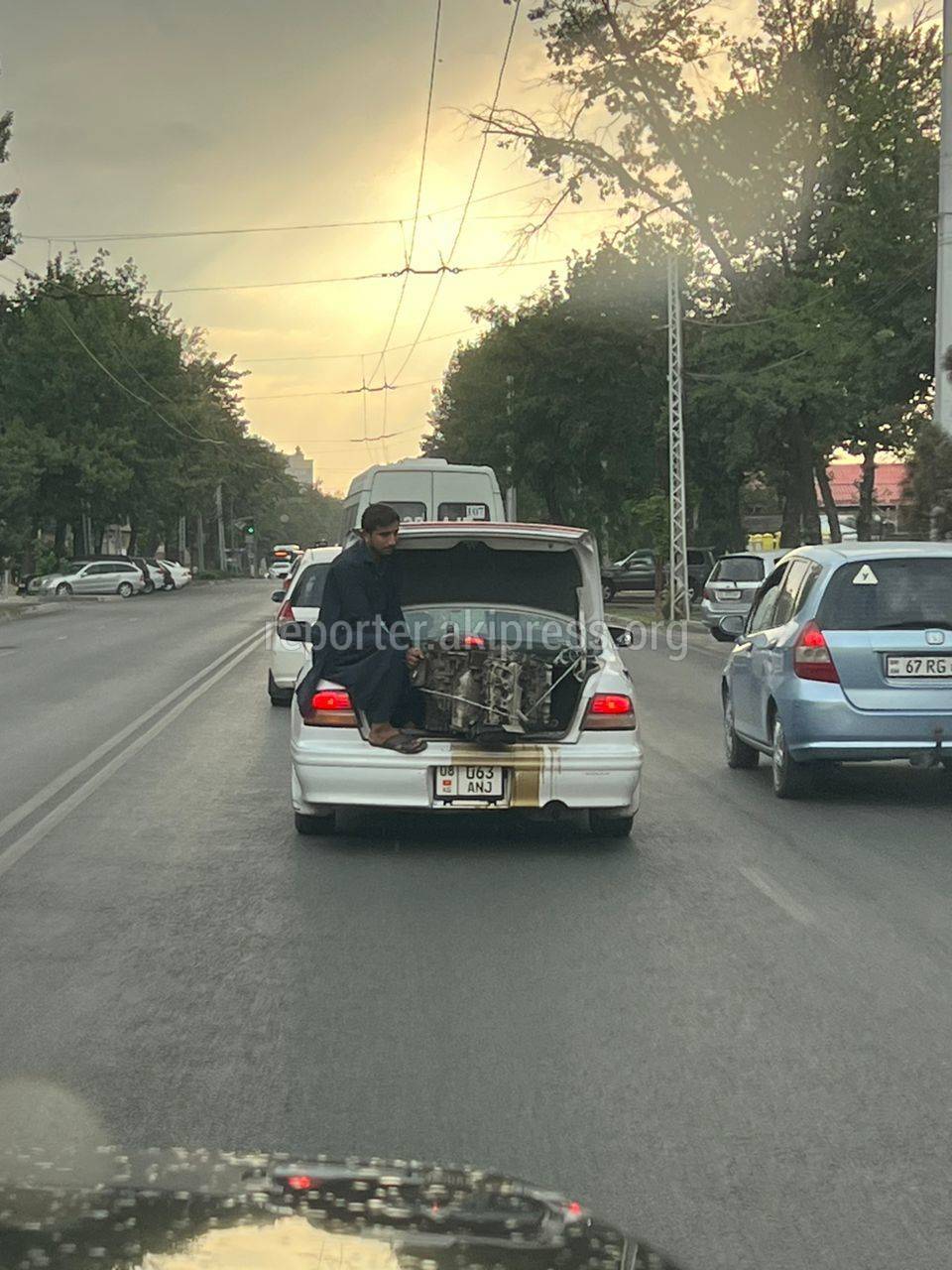 Мужчина едет в багажнике машины, а в руках у него двигатель авто. Фото